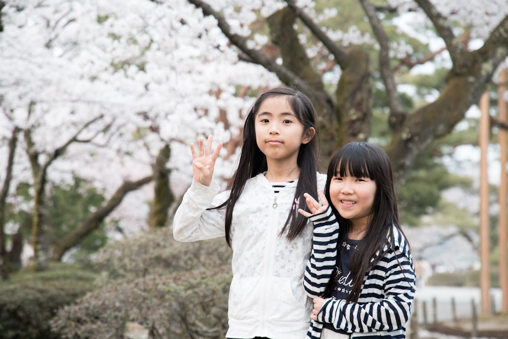 two girls standing behind brown tree with white leaves