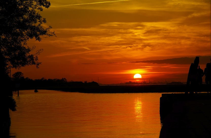 A golden sunset over the calm Gulf Coast waters with silhouettes of families playing on the beach.