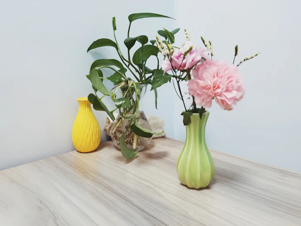 An elegant tabletop arrangement with vibrant seasonal flowers and greenery in a simple ceramic vase on a wooden dining table.