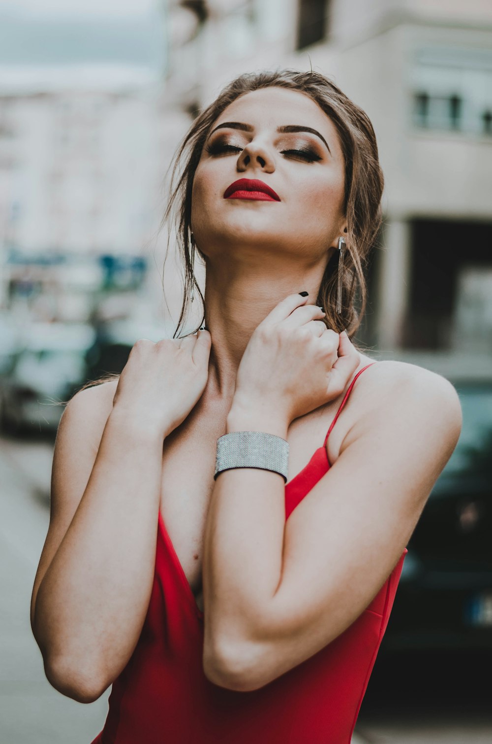 woman holding her neck while closed eyes near building