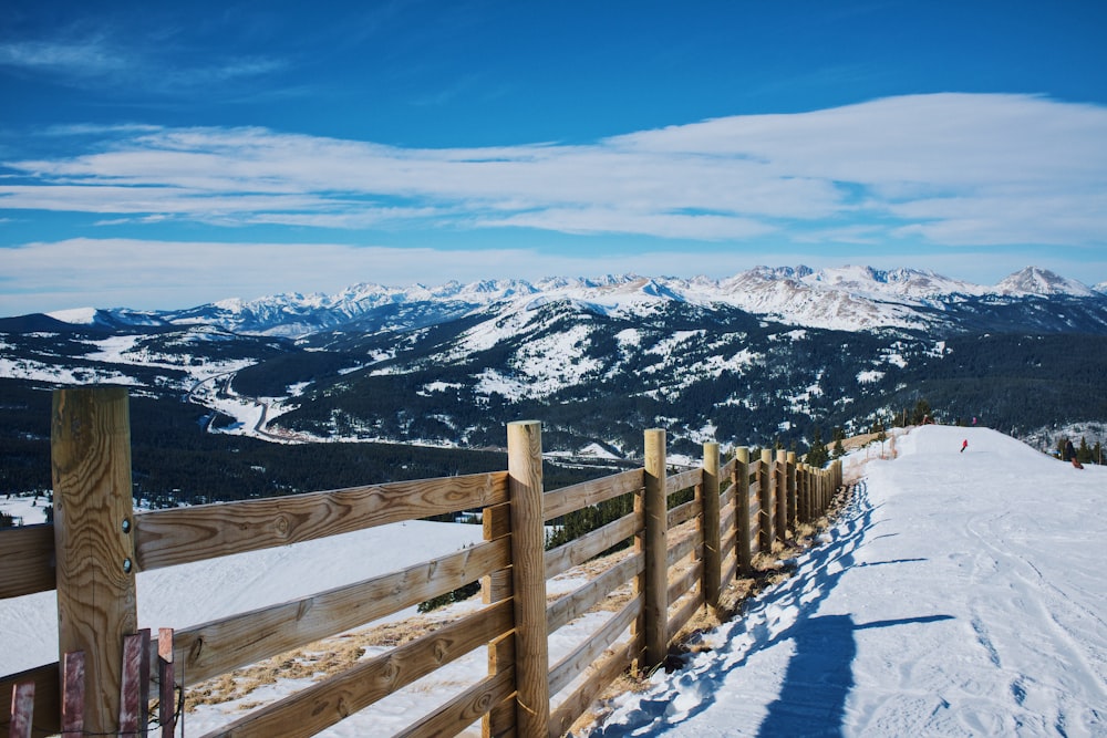Campo de nieve y valla de madera marrón cerca de la montaña durante el día