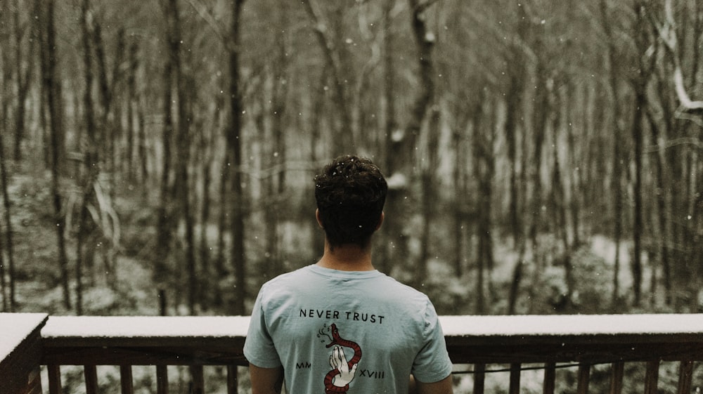 man wearing gray T-shirt standing beside brown wooden railing during snowy day