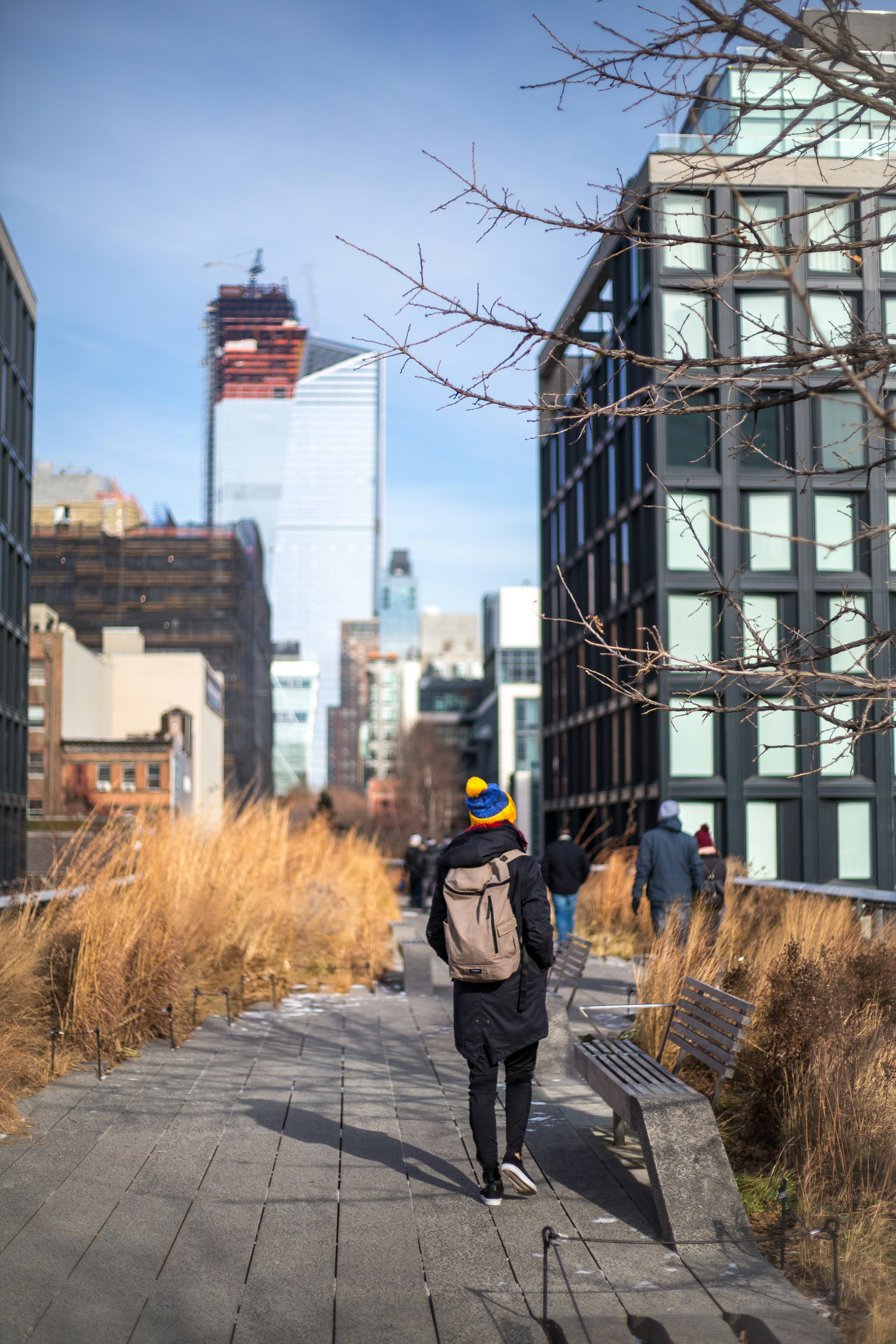 person wearing winter clothes with brown backpack walking on gray pathway outdoors during day