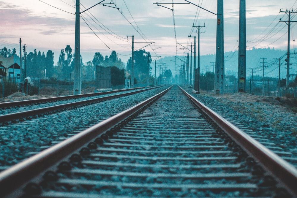 gray electricity post lined near brown metal train rail during daytime