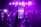 A lively party scene captured through the lens of a smartphone, with a crowd of people dancing under vibrant purple stage lights. The phone in the foreground mirrors the scene with its own display, emphasizing the integration of digital technology in social events.