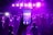 A lively party scene captured through the lens of a smartphone, with a crowd of people dancing under vibrant purple stage lights. The phone in the foreground mirrors the scene with its own display, emphasizing the integration of digital technology in social events.