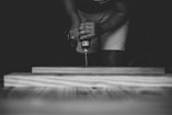 person drilling brown wooden board using power drill