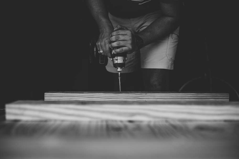 person drilling brown wooden board using power drill