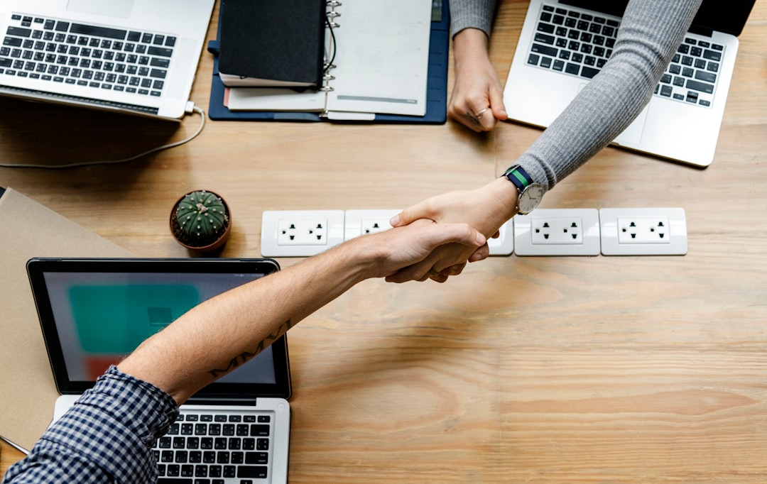 two person handshaking in front of MacBook Pro