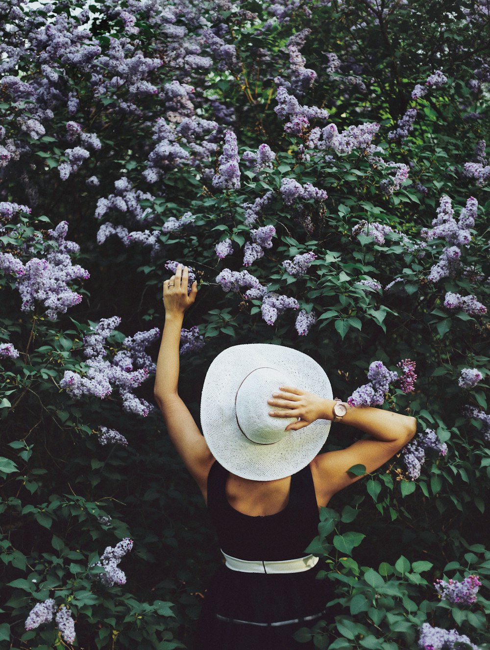 mujer con blusa negra sin mangas y sombrero de sostenimiento y flores moradas rodeadas