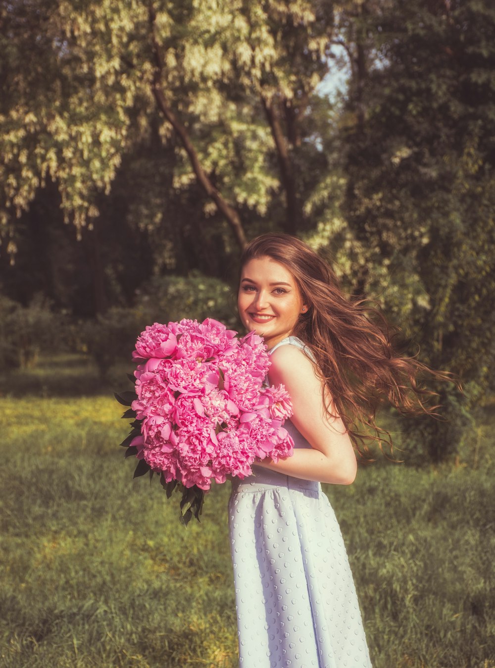 Mujer sosteniendo ramo de flores rosas sonriendo durante el día