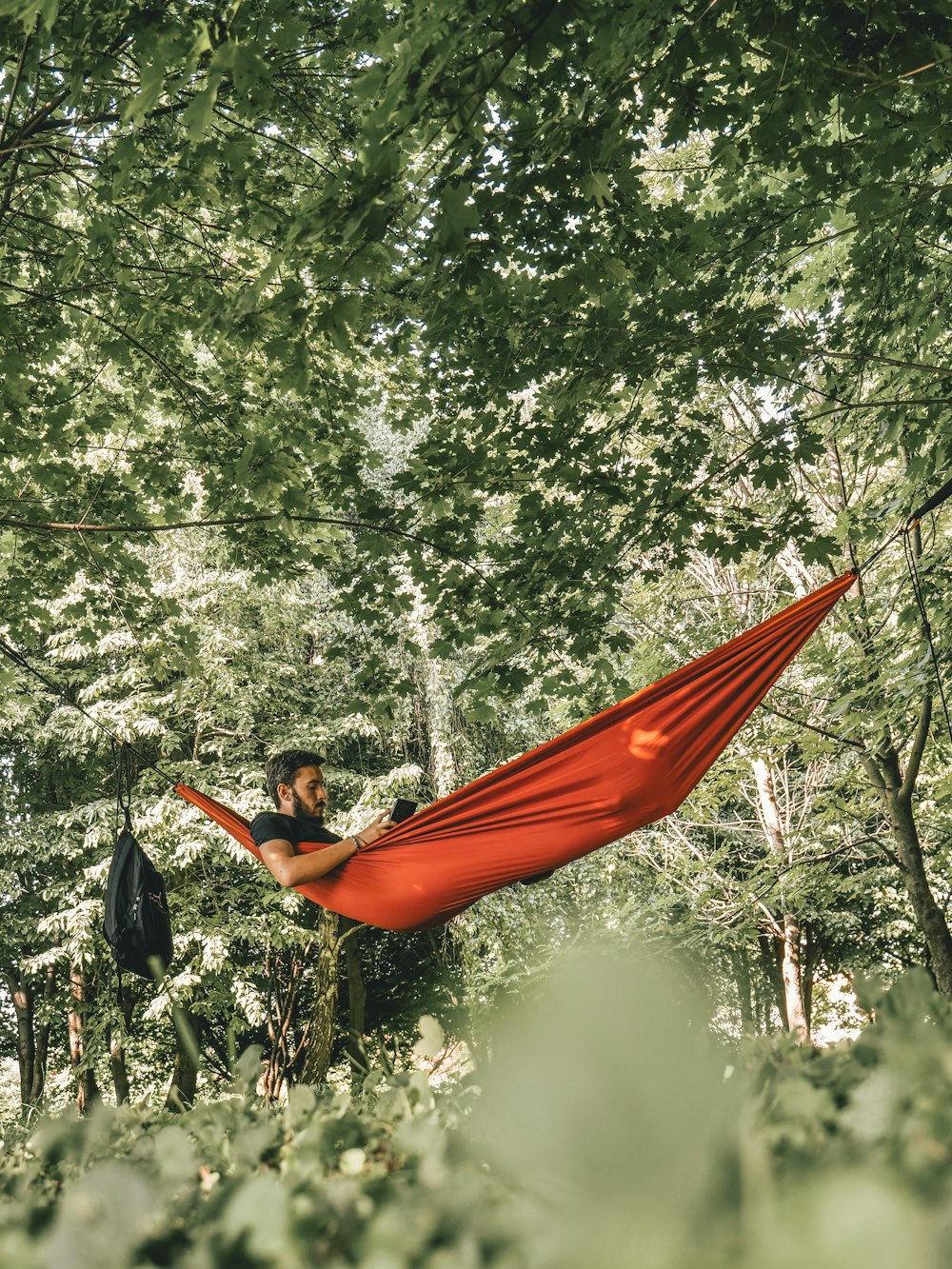 man on red hammock surrounded by trees during daytime