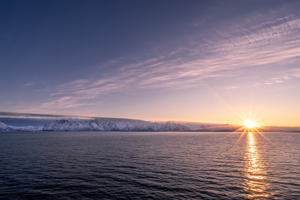 calmly body of water over mountain under blue sky at sunset