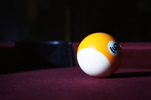 A yellow and white billiard ball with the number ten is lying on a burgundy pool table. The background is dark, emphasizing the ball.