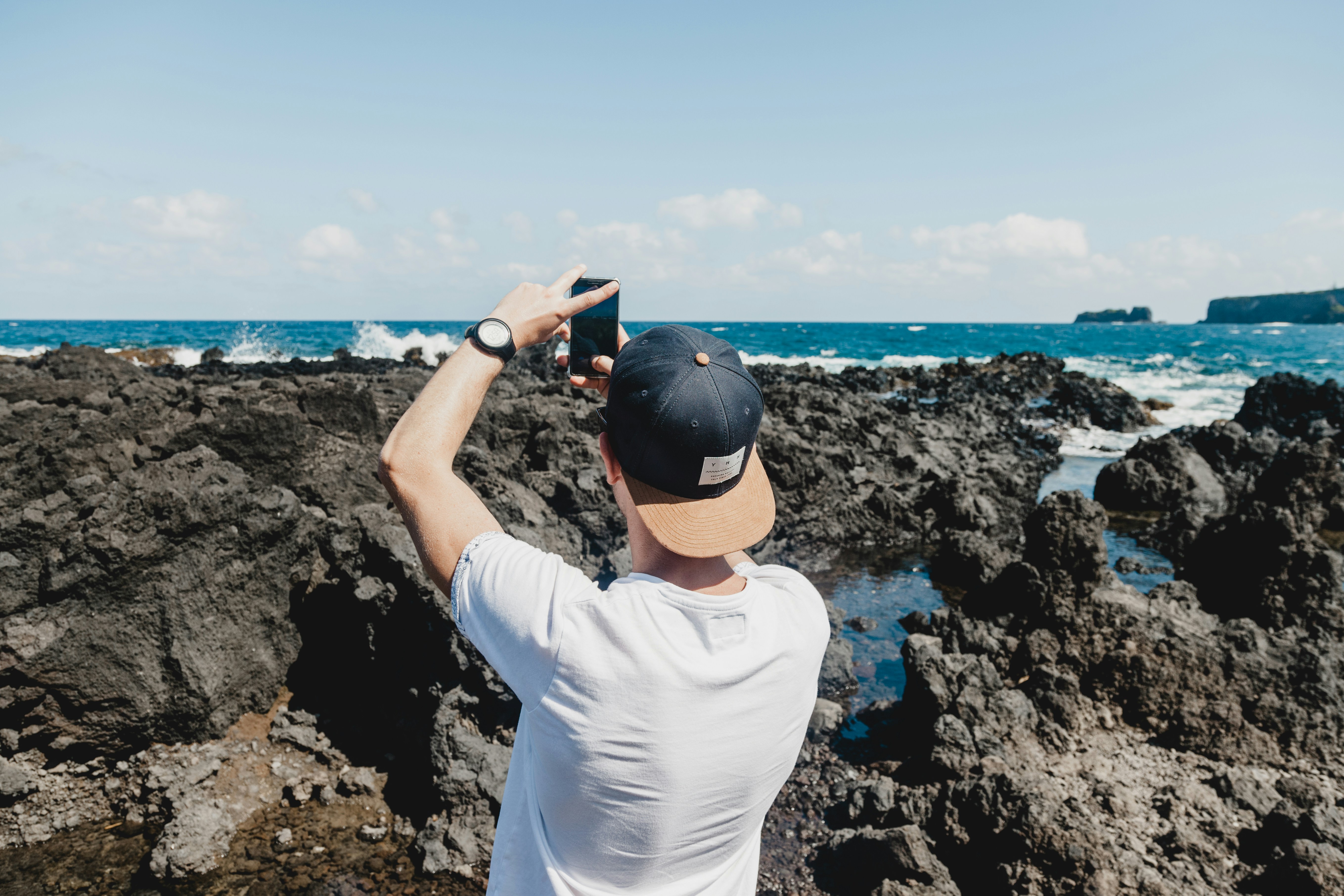 man holding black smartphone while taking a photo of open sea maui zoom background