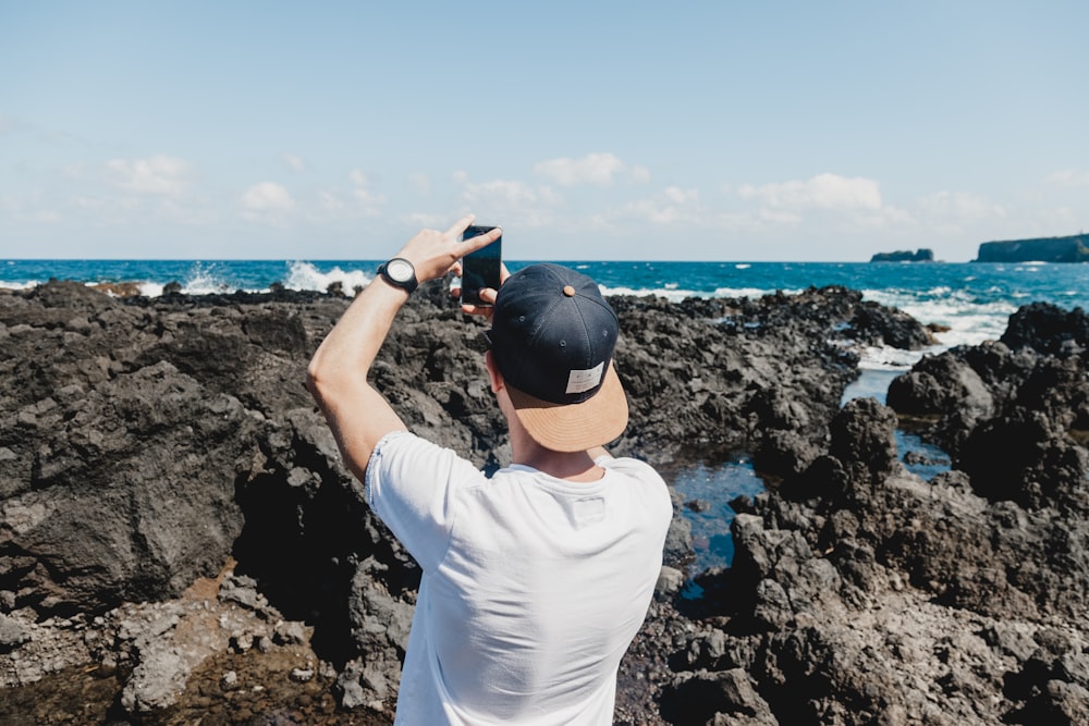 hombre sosteniendo un teléfono inteligente negro mientras toma una foto de mar abierto