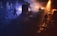 A live music performance with a band on stage, surrounded by a smoky atmosphere. The lighting is dramatic with warm spotlights illuminating the band members, creating a contrast with the dark, shadowy background.