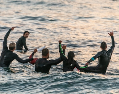 people wearing black wetsuits in body of water
