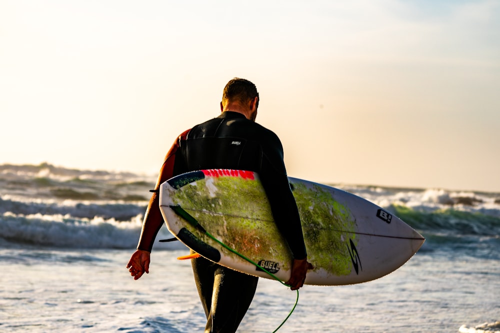 homem carregando prancha de surf branca enquanto caminha em direção ao mar com ondas durante o dia