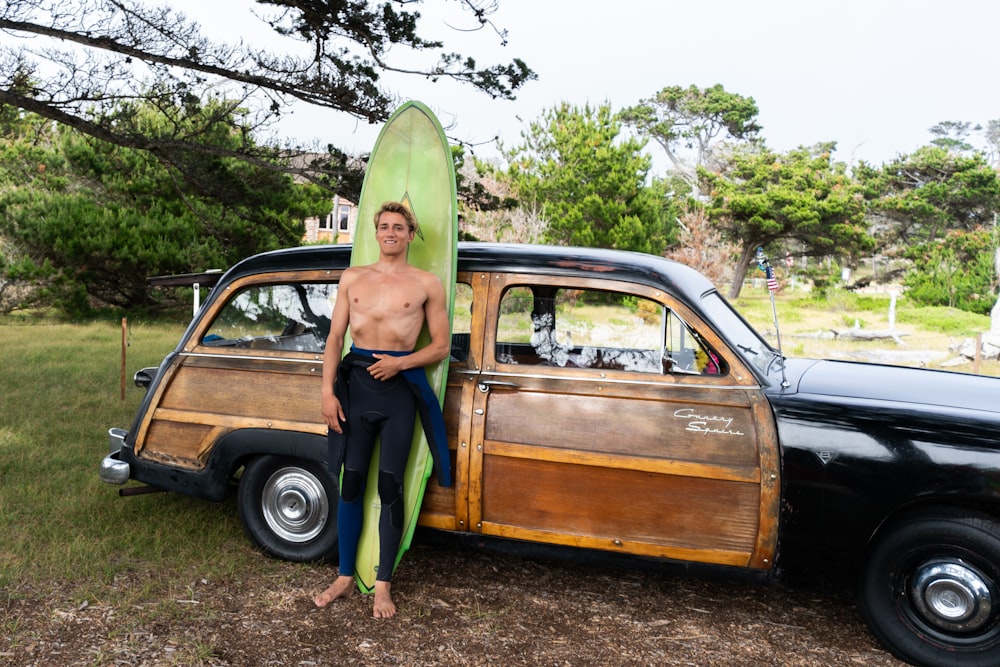 homem em pé ao lado do carro encostado em prancha de surf verde