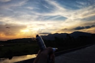 A hand holding a vape pen against a sunset backdrop.