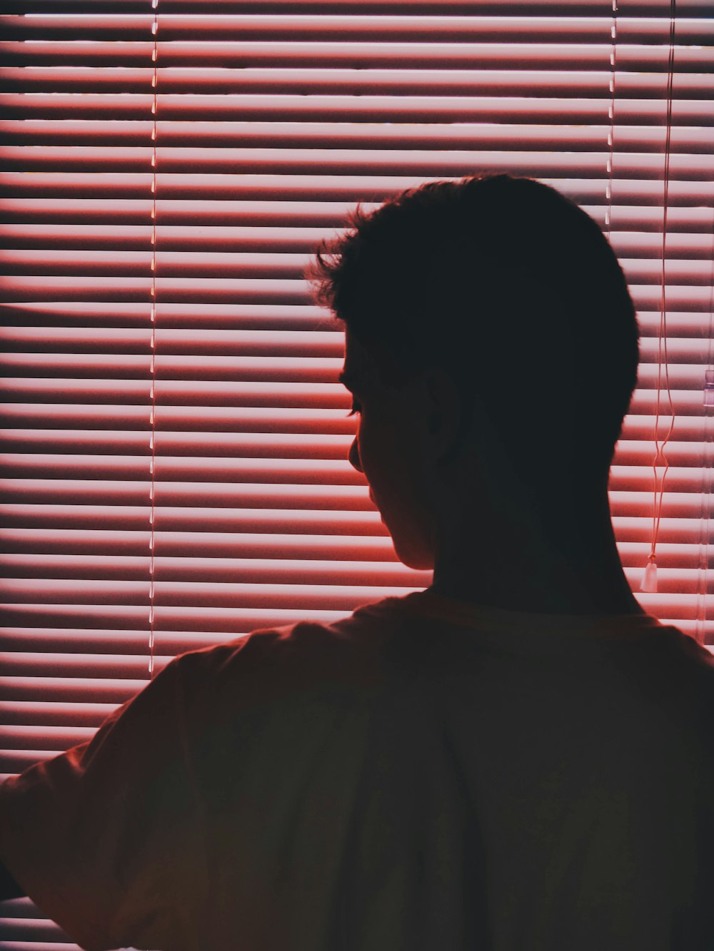 man in white crew-neck t-shirt near pink vinyl blinds