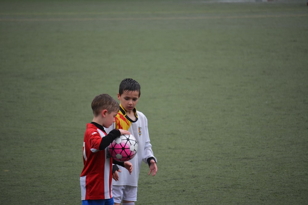boy holding soccer ball beside other ball on soccer field