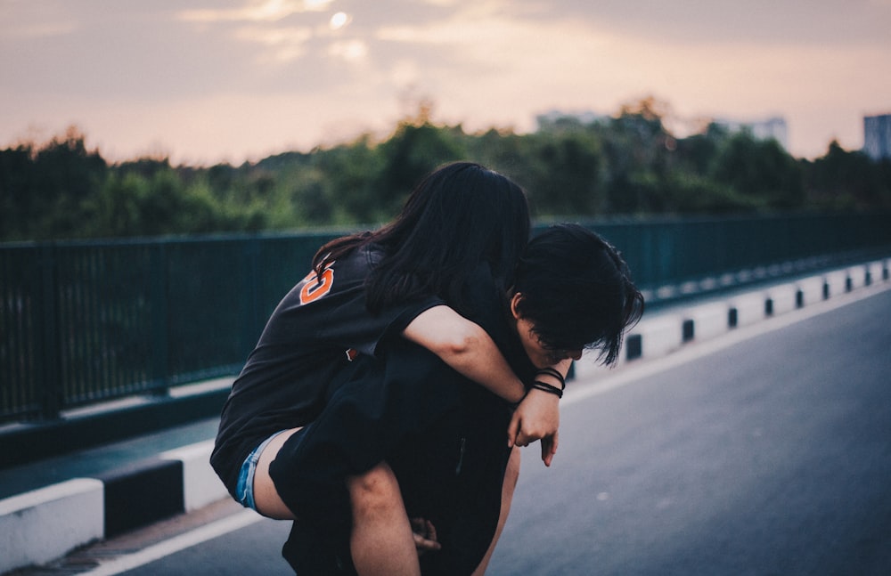 donna piggyback sull'uomo in piedi sulla strada di cemento grigia durante il giorno