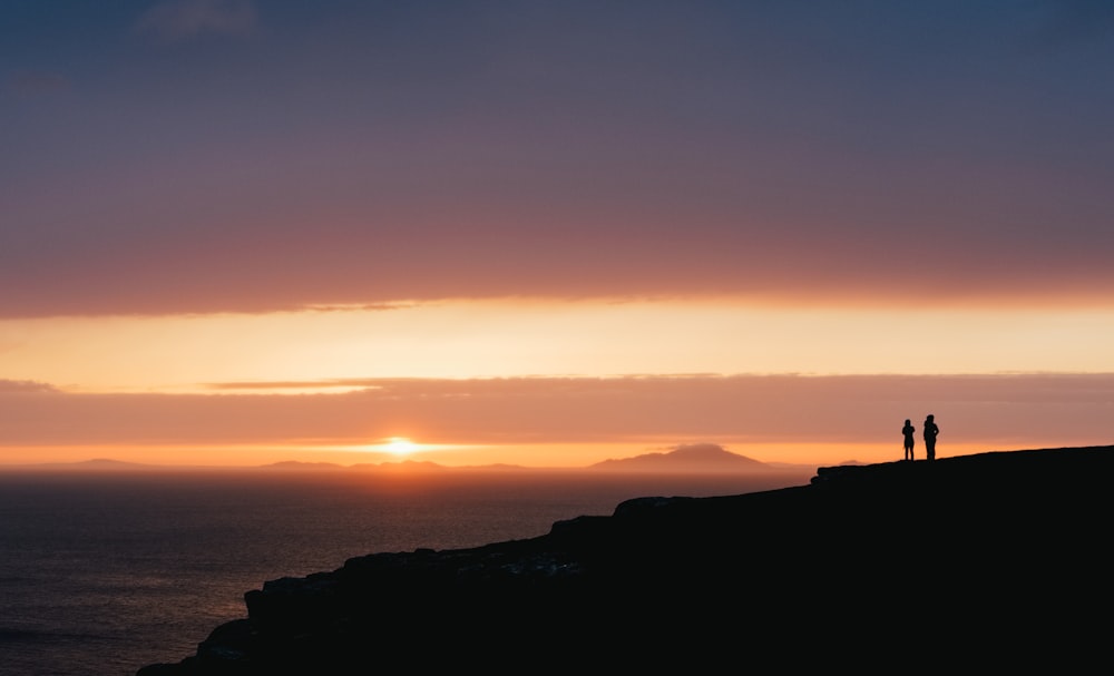 silhouette of two person standing on hills during golden hour