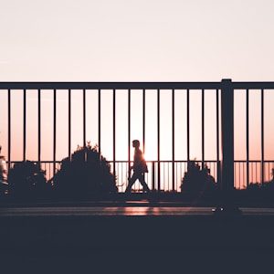 silhouette of person walking on roadside during sunset