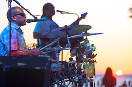 Musicians passionately playing Jamuna Band drums during an outdoor concert at sunset.