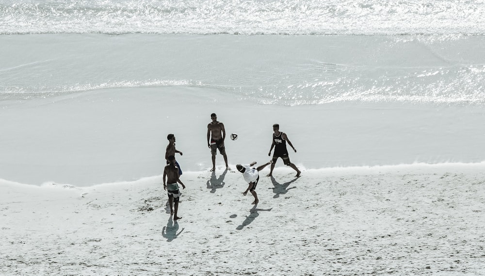 five man playing soccer on shoreline