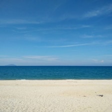 A serene beach with golden sand and clear blue water under a bright sky.