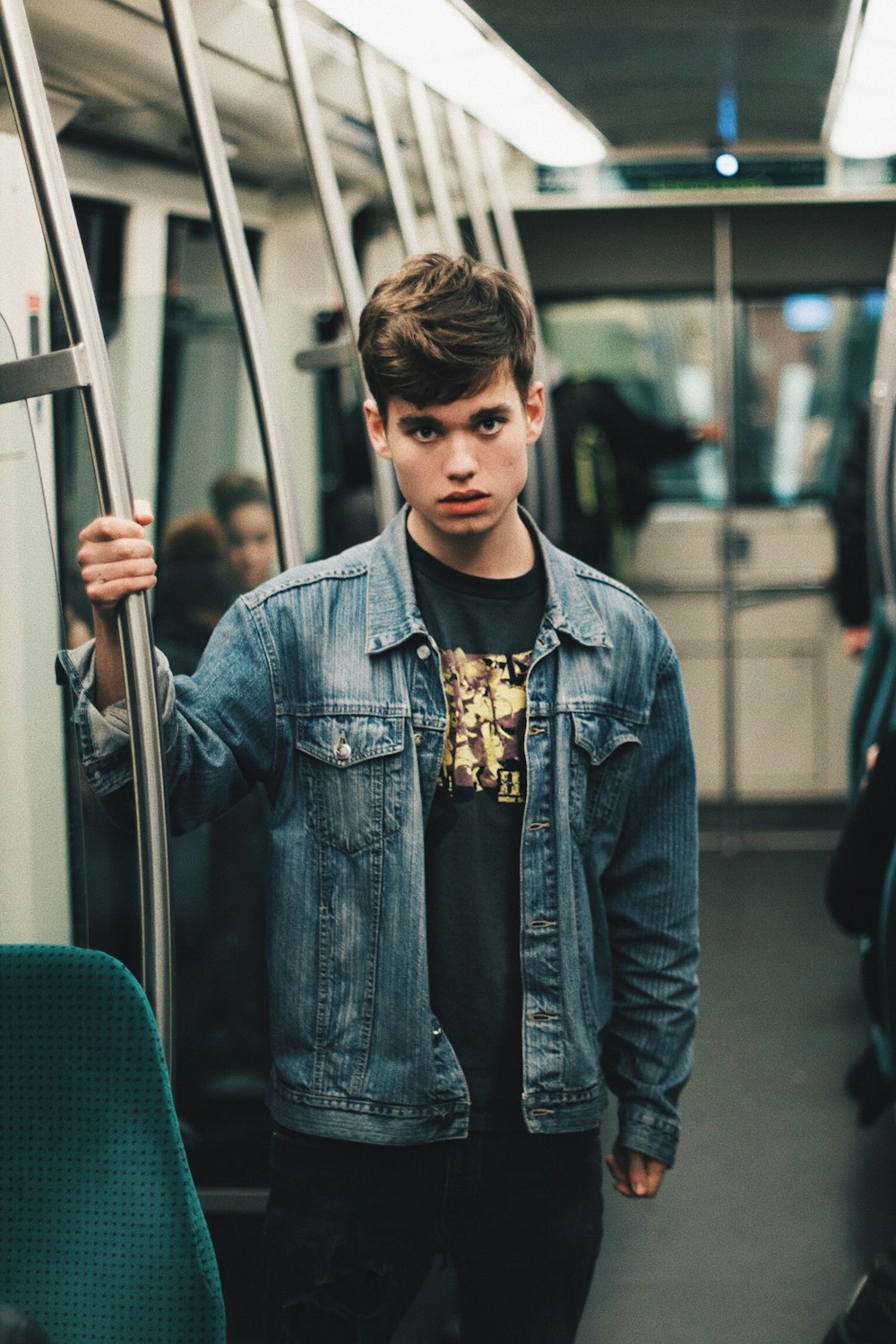 man wearing blue denim jacket standing inside train