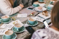 Children and adults sharing smiles and quiet conversations around a picnic table with pastel-colored mugs.