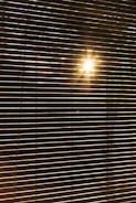 Horizontal blinds partially open with sunlight streaming through, creating a pattern of light and shadow across the blinds.