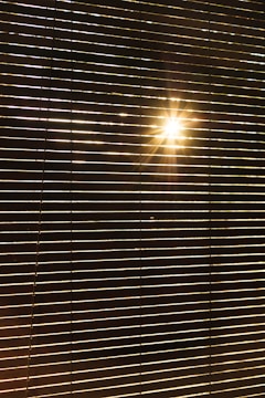 Horizontal blinds partially open with sunlight streaming through, creating a pattern of light and shadow across the blinds.