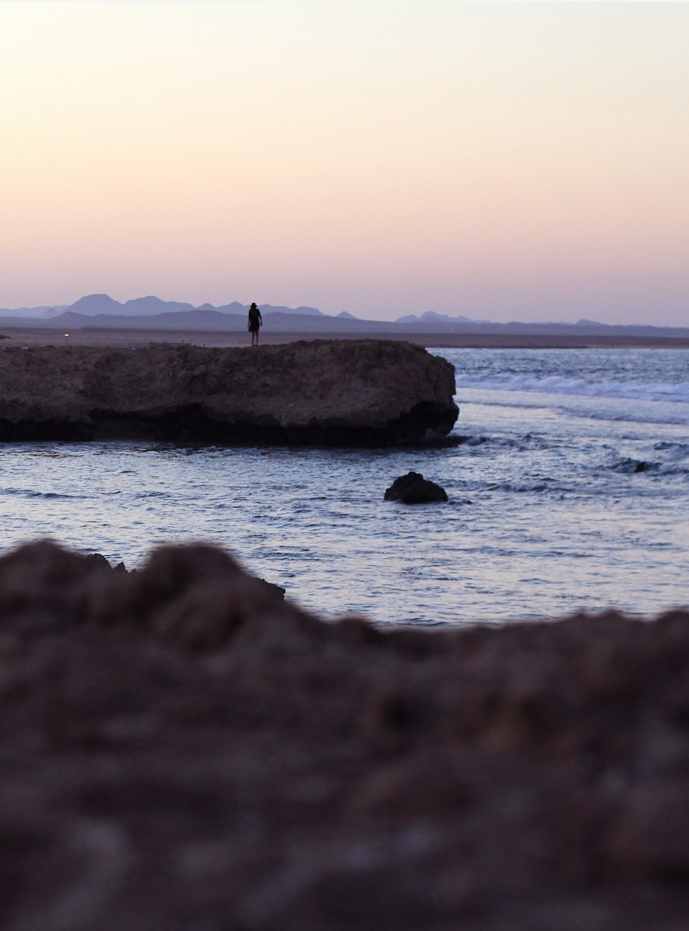 person standing on cliff near body of water