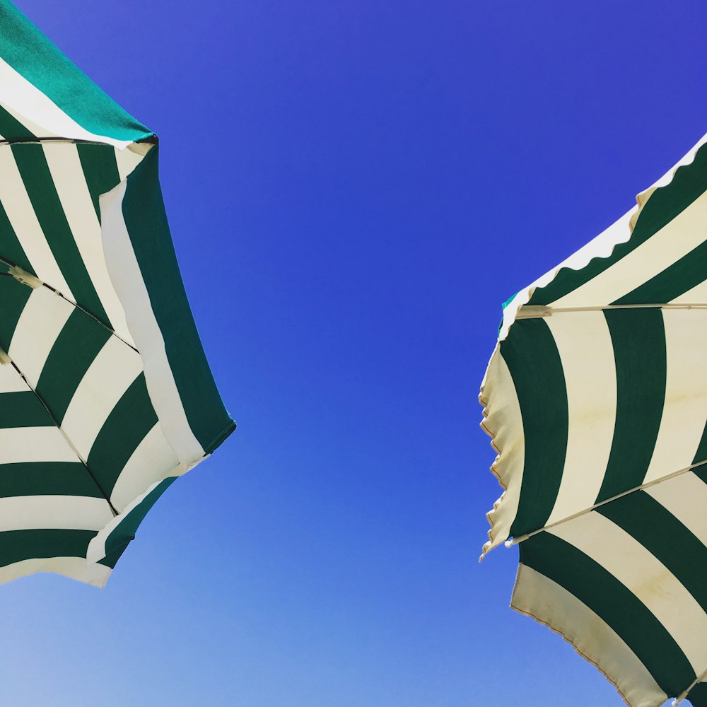 Fotografie aus der Wurmperspektive von zwei grün-weißen Sonnenschirmen unter blauem Himmel während des Tages