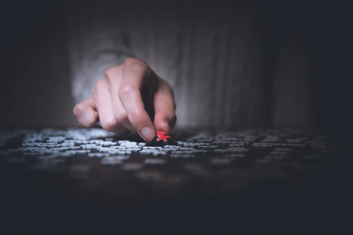 A hand holding a red jigsaw puzzle piece up to the light.