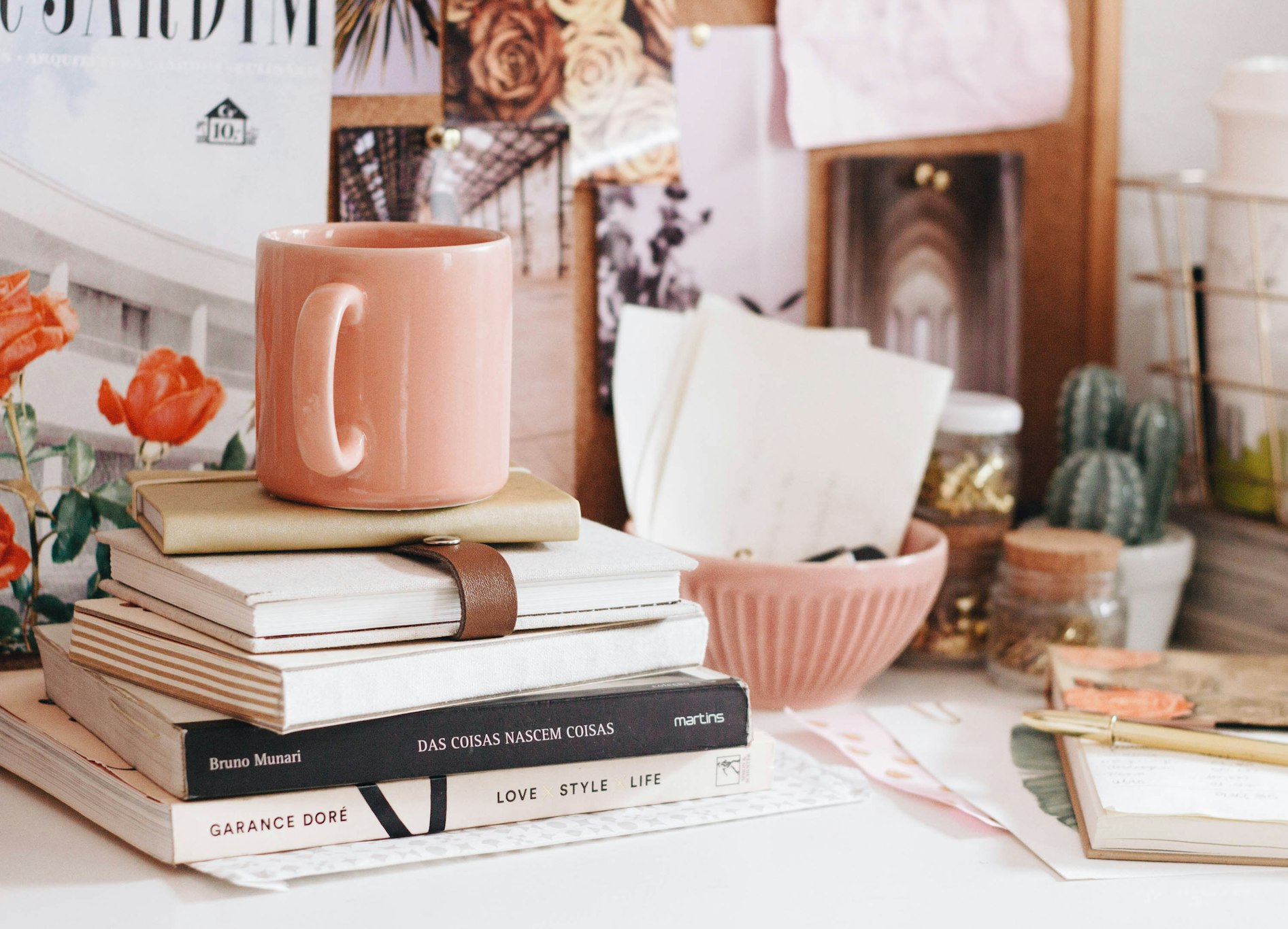 A stacked pile of assorted books with a peach coloured coffee cup on top.