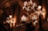 An opulent interior with ornate chandeliers casting a warm glow. The architecture features grand columns and intricate ceilings, creating a sense of luxury and elegance. The space feels historic with rich decorative elements.