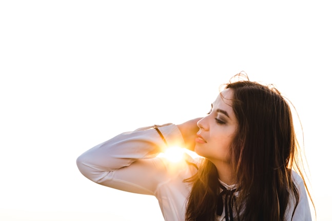 Close-up of a woman gently touching her shiny, healthy hair in soft natural light.