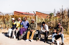 six men sitting on bench in front barbed wire fence