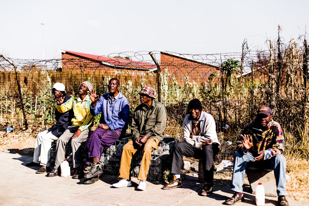 six men sitting on bench in front barbed wire fence