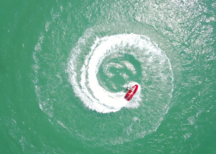 aerial photography of red personal watercraft circling on water at daytime