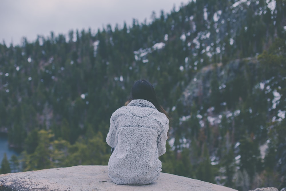 woman in white long-sleeved top sitting on rock