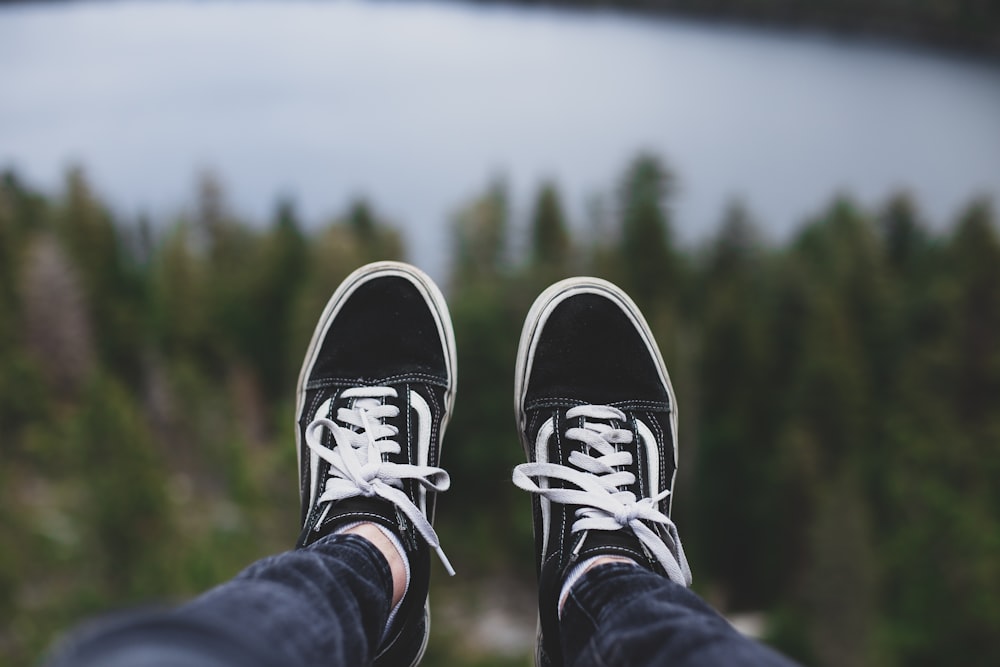 a person wearing black and white shoes standing in front of a lake