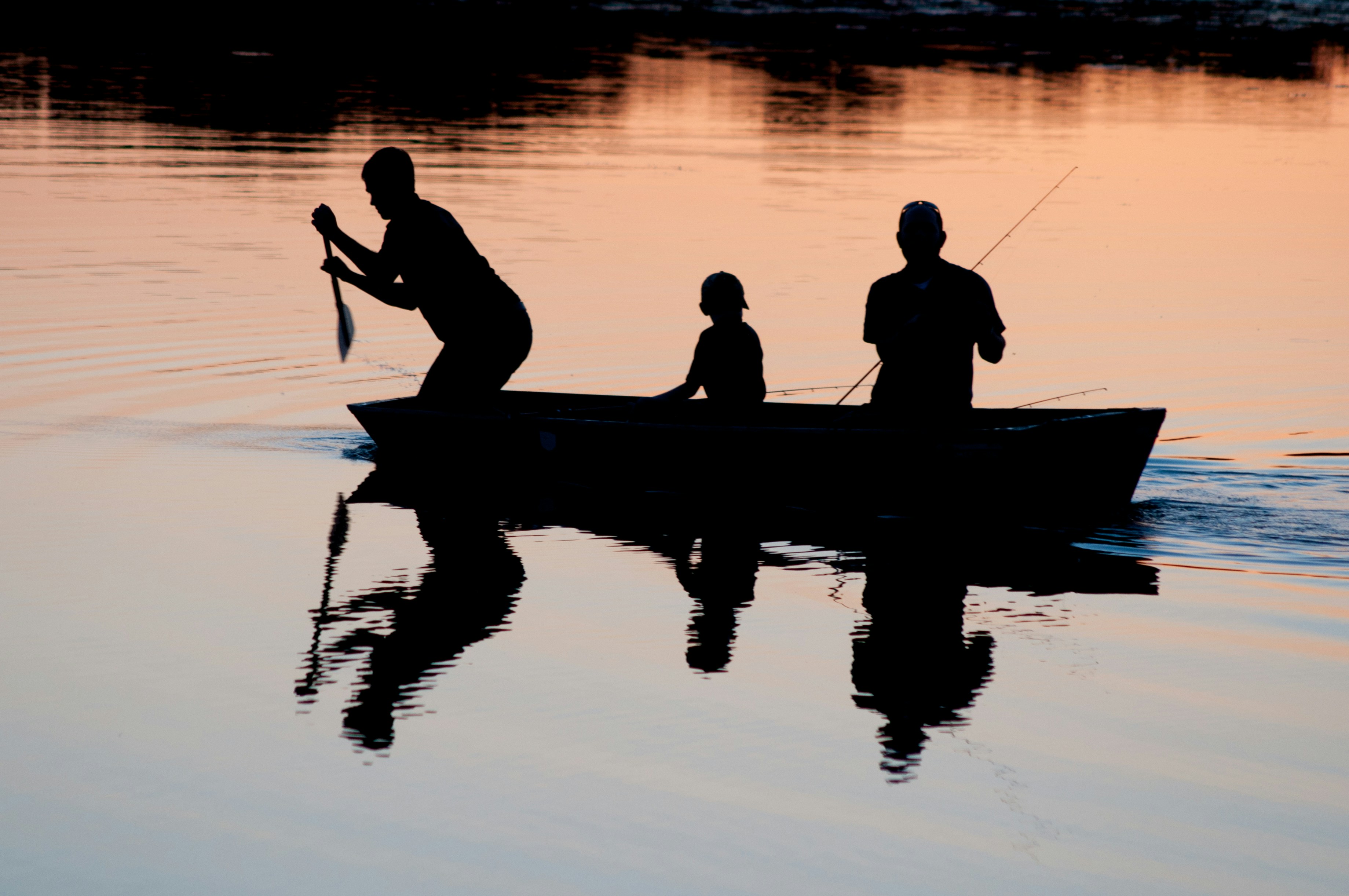 3 People in a boat on a lake at sunset fishing