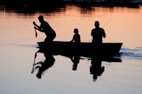 silhouette of three person riding on boat on body of water